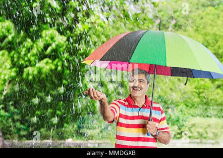 Felice Senior uomo sotto l'ombrello putting-out invece sentire le gocce di pioggia palm Park Foto Stock