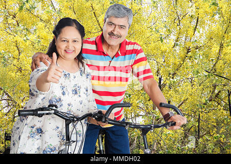 Felice coppia Senior seduta ciclo e mostra Thumbs up Godetevi At-Park Foto Stock