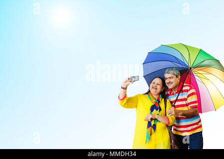 Felice coppia Senior sotto ombrellone tenendo Selife foto fotocamera all'aperto Foto Stock