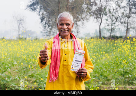 Un vecchio uomo Azienda Aadhaar-Card mentre mostra Thumbs up villaggio rurale Foto Stock