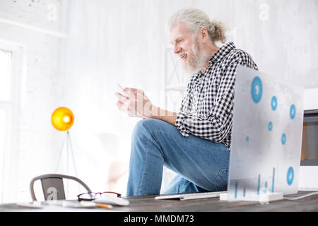 Senior piacevole uomo seduto sul tavolo e i messaggi di testo Foto Stock