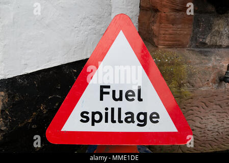 Il bianco e il rosso triangolare di sicurezza stradale le fuoriuscite di carburante in segno di avvertimento testo nero su sfondo bianco contro la parete con spazio di copia Foto Stock
