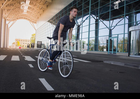 Giovane uomo equitazione sulla bicicletta in una strada di città. Uomo sulla bicicletta blu con ruote bianco, grande specchio sullo sfondo di Windows Foto Stock