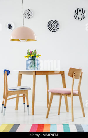 Colorata sala da pranzo interno con un tavolo e sedie, striped rug, pastello lampadario e piastre di sospensione sulla parete Foto Stock