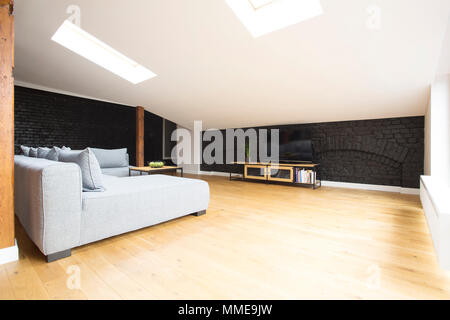 Spazioso soggiorno interno con nero, muro di mattoni e grigio divano ad angolo Foto Stock