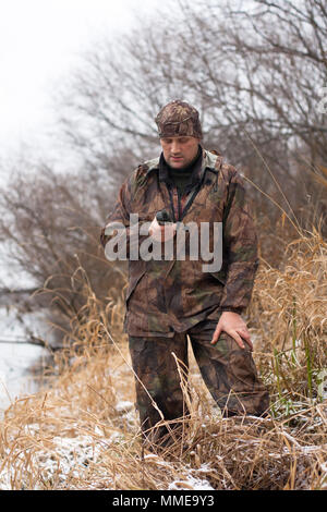 Uomo in camuffamento cercando su GPS Navigator sulla riva del fiume Foto Stock