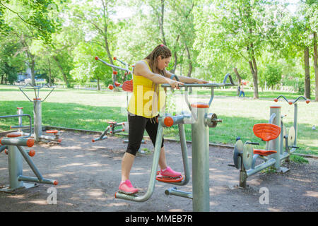 La donna incinta è fare gli esercizi all'aperto sulla macchina fitness in un parco. Foto Stock