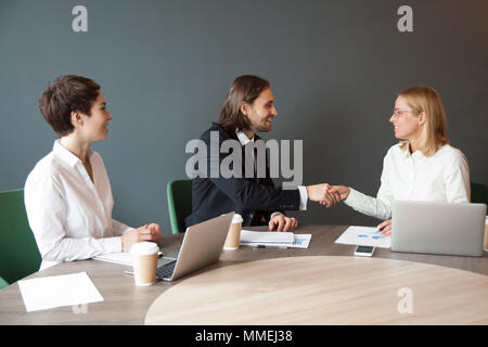 Imprenditore sorridente agitando la mano del partner di sesso femminile al gruppo di soddisfare Foto Stock