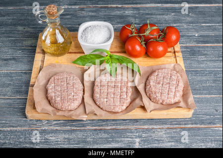 Hamburger di pollo cotolette su una tavola di legno con pomodorini e spezie Foto Stock