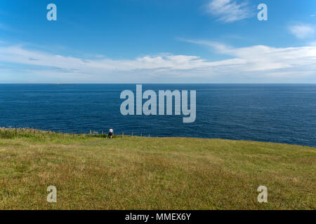 Highland walker per le cime della scogliera a testa Duncansby che guarda al Mare del Nord e di Pentland Skerries Lighthouse appena al di sotto dell'orizzonte. Foto Stock