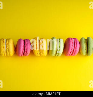 Colorate dolci cotti al forno di farina di mandorle con crema su sfondo giallo, dessert macarons risiede in una riga nel mezzo Foto Stock