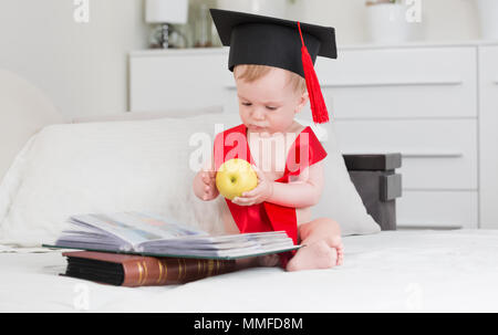 Dieci mesi baby boy in graduazione hat la lettura di libri e di azienda big apple Foto Stock