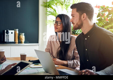 Colleghi di lavoro parlare insieme seduti a un tavolo per riunioni in un ufficio avente una riunione Foto Stock