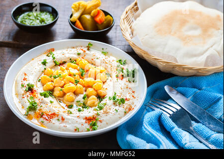 Hummus israeliano insalata cremosa di colore bianco sulla ciotola con ceci, olio d'oliva, prezzemolo e paprica. Servita con pane su un tavolo di legno. Foto Stock