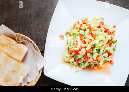 Insalata israeliana sulla piastra bianca. Serviti con pane tostato su sfondo di legno. Foto Stock