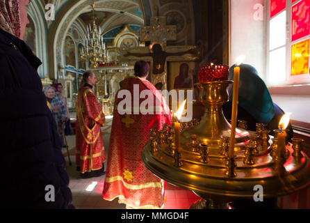 KAZAN, Russia - 11 Maggio 2018: Nikolsky cattedrale ortodossa - candele accese sul supporto di fronte a due sacerdoti ortodossi in preghiera Foto Stock