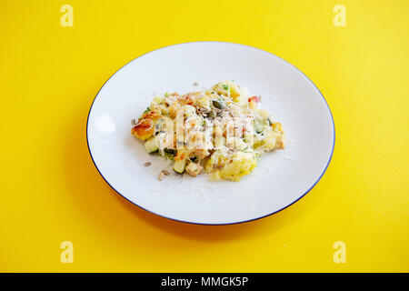 Piastra bianca con patate, verdure e formaggio sulla tabella di colore giallo Foto Stock