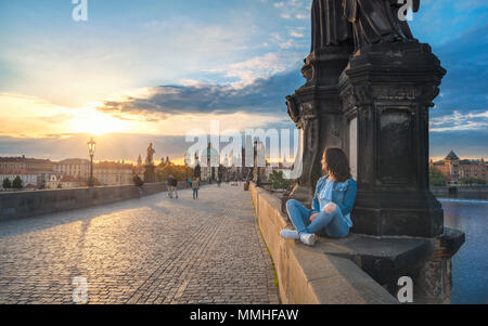 Bruna giovane donna seduta rilassata sul Ponte Carlo pareti, sul fiume Vltava, ammirando il tramonto sulla città di Praga, nella Repubblica Ceca. Foto Stock