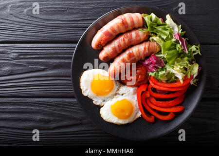 In casa salsicce fritte avvolto in pancetta, uova, salsa e insalata fresca di close-up su una piastra superiore orizzontale vista da sopra Foto Stock