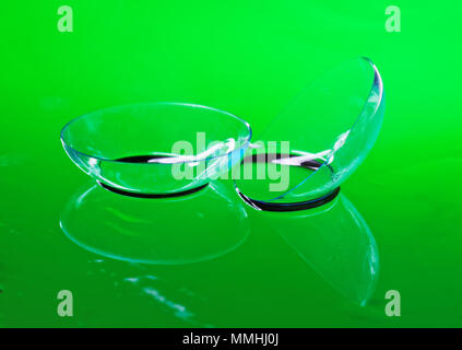 Trasparente lenti a contatto per la correzione di visione giacciono su uno specchio superficie bagnata. Sfondo verde Foto Stock