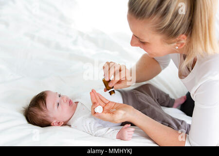 Giovane e bella madre sta dando il suo grazioso baby figlia globuli omeopatici Foto Stock