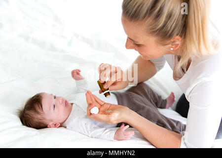 Giovane e bella madre sta dando il suo grazioso baby figlia globuli omeopatici Foto Stock