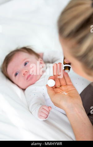 Giovane e bella madre sta dando il suo grazioso baby figlia globuli omeopatici Foto Stock