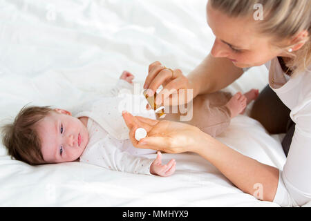 Giovane e bella madre sta dando il suo grazioso baby figlia globuli omeopatici Foto Stock