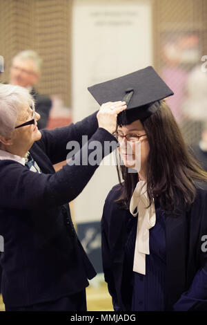 Femmina caucasica coppia graduate essendo vestito di cap & abito (Mortarboard) in fase di preparazione per il Diploma di Master cerimonia di laurea Università di Chester Foto Stock