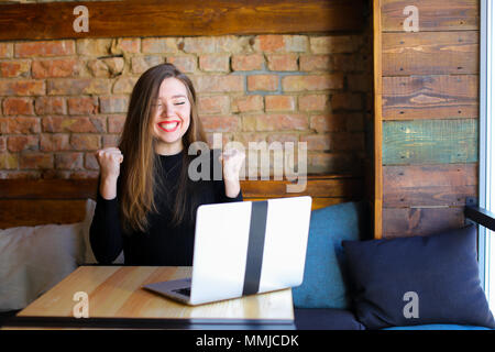 Lucky girl godendo di vincere le scommesse online dal computer portatile presso il cafe. Foto Stock