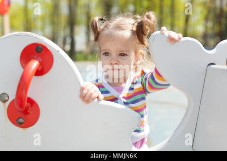 Una bambina con due code è vestito in un colorato striped jacket è giocare nel parco giochi estate kid tempo libero Foto Stock