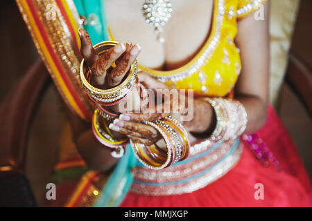 Close-up shot indiana di sposa con belle saree in camicetta giallo e rosso lehenga mettendo un sacco di glitter bracciali (bangle) a portata di mano con mehnd Foto Stock