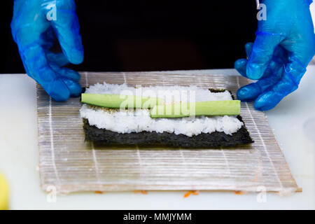 Preparazione di rotoli in un sushi bar. Un cuoco professionista indossando guanti blu è la preparazione tradizionale giapponese del cibo. Riso, cavolo riccio di mare, il cetriolo. Foto Stock