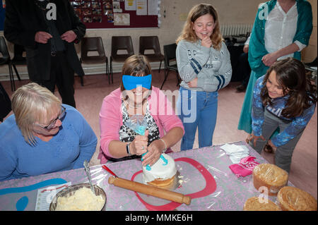 I residenti di stoppino in Littlehampton, West Sussex, Regno Unito celebrare le nozze reali tra il principe Harry e Meghan Markle prendendo parte ad un Royal Wedding sfida. Durante la sfida, i concorrenti hanno dovuto fare una torta di nozze, dress up e applicare il trucco mentre blindfolded o avere le mani legate insieme. In foto: gli occhi bendati, un concorrente tenta di decorare la torta nuziale. Foto Stock