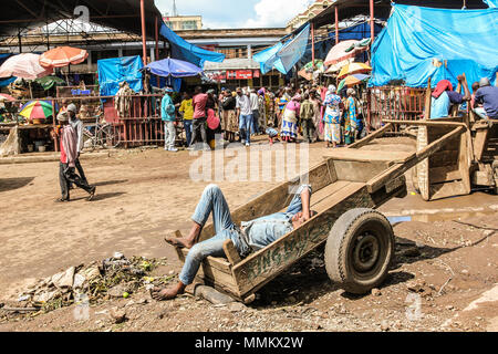 Arusha, Tanzania Africa - Gennaio 2, 2013: uomo disteso su un carrello di legno dorme in un mercato della città. Questi mercati africani sono pieni di colori e di persone che vendono i loro prodotti locali e loro coltivano frutta e verdura Foto Stock