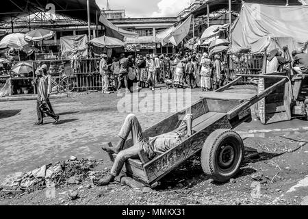 Arusha, Tanzania Africa - Gennaio 2, 2013: uomo disteso su un carrello di legno dorme al mercato in città Foto Stock