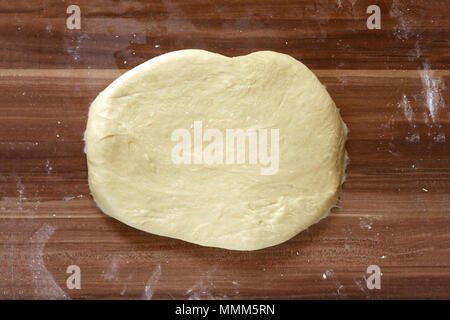 Rendendo la pizza fatta in casa in un paese cucina con una vista aerea di pasta laminata per la base con una laminazione di legno pin su carta forno su un vecchio wo Foto Stock