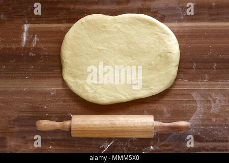 Rendendo la pizza fatta in casa in un paese cucina con una vista aerea di pasta laminata per la base con una laminazione di legno pin su carta forno su un vecchio wo Foto Stock