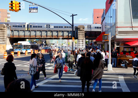 Persone che attraversano la strada nel centro di Flushing nel Queens, New York, NY. Sullo sfondo, traffico di treni e autobus, maggio 2018. 法拉盛, 法拉盛華埠, 華裔美國人, 紐約 Foto Stock