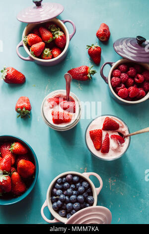 Strawberry Cheesecake ,su uno sfondo blu e vista dall'alto di frutti di bosco , all'interno della ceramica cocotte colorate, mirtilli, fragole, lamponi, piatto Foto Stock