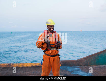 Marinaio AB o Bosun sul ponte della nave in mare aperto o nave , indossando PPE equipaggiamento protettivo personale - casco, tuta, giubbotto di salvataggio, occhiali. Egli detiene VH Foto Stock