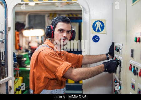 Ingegnere Marine officer avvia o arresta il motore principale o generatori di nave in sala motori. I marinai di lavoro. Egli indossa una protezione per le orecchie. Foto Stock