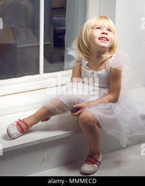 Ragazza 3 anni in un bellissimo abito bianco vicino alla finestra invernale Foto Stock