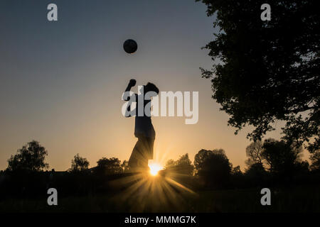 Un ragazzo pratica la sua abilità calcistiche come il sole scende, giocare a calcio fino al buio Foto Stock