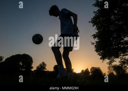 Un ragazzo pratica la sua abilità calcistiche come il sole scende, giocare a calcio fino al buio Foto Stock