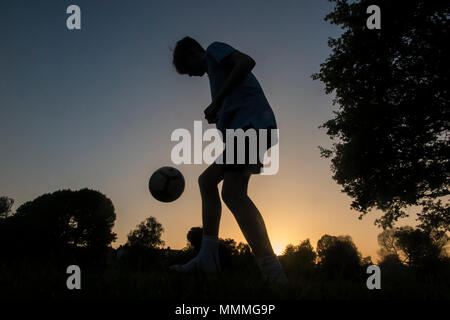 Un ragazzo pratica la sua abilità calcistiche come il sole scende, giocare a calcio fino al buio Foto Stock