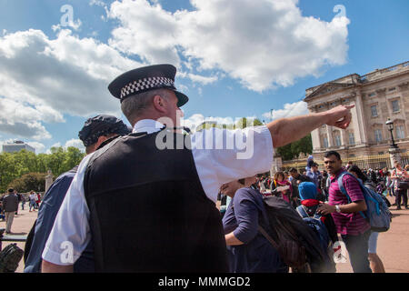 Un giorno di primavera fuori Buckingham Palace e un poliziotto assiste il turista con le direzioni Foto Stock