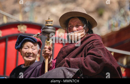 Pellegrino tibetano gira una ruota di preghiera al di fuori della sacra Scrittura Bakong Stampa Monastero a Dege, Sichuan, in Cina Foto Stock