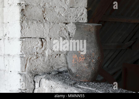 Vecchio e rustico e polveroso marrone vaso in piedi vicino al bianco muro di mattoni Foto Stock