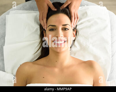 Vista dall'alto di giovani caucasici donna sorridente ricevere un massaggio della testa in un centro termale. Paziente di sesso femminile è di ricevere il trattamento dal terapista professionale. Foto Stock